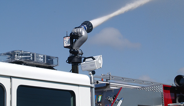 An extend a gun attached to a deck mounted monitor flows water from the top of a fire apparatus