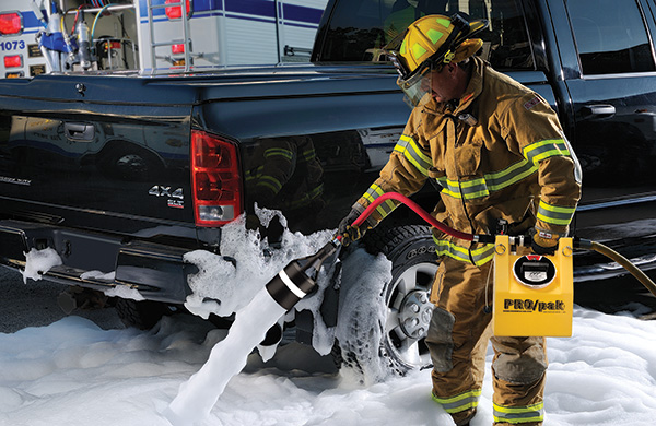 Firefighter uses a PRO/pak portable foam system to apply a foam blanket near a pickup truck