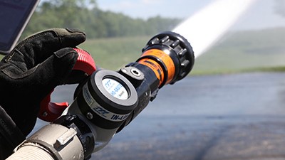 A firefighter holds a TFT Metro nozzle with a SHO-GAUGE inline bluetooth pressure gauge attached.